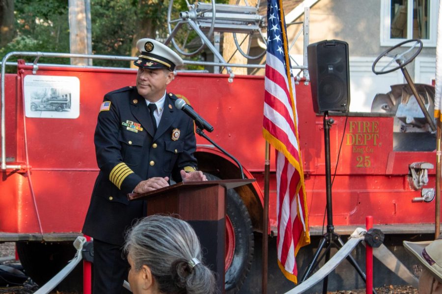 Evanston Fire Chief Paul Polep speaks in front of a red fire truck. Polep is wearing a white hat and black suit.