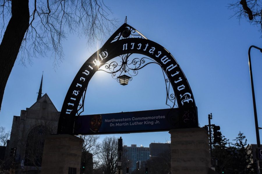 Weber Arch amid a blue sky. The sun shines through one of the letters engraved on the arch.