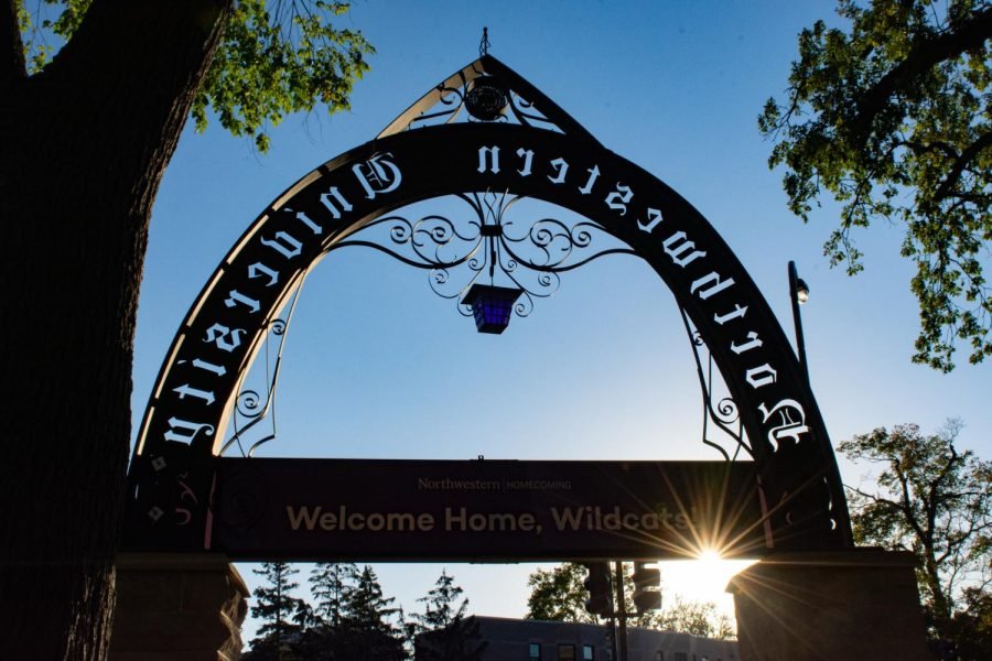 Photo is of Northwestern’s arch, with a purple banner across with the text, “Welcome Home, Wildcats!” The sun shines under the banner.