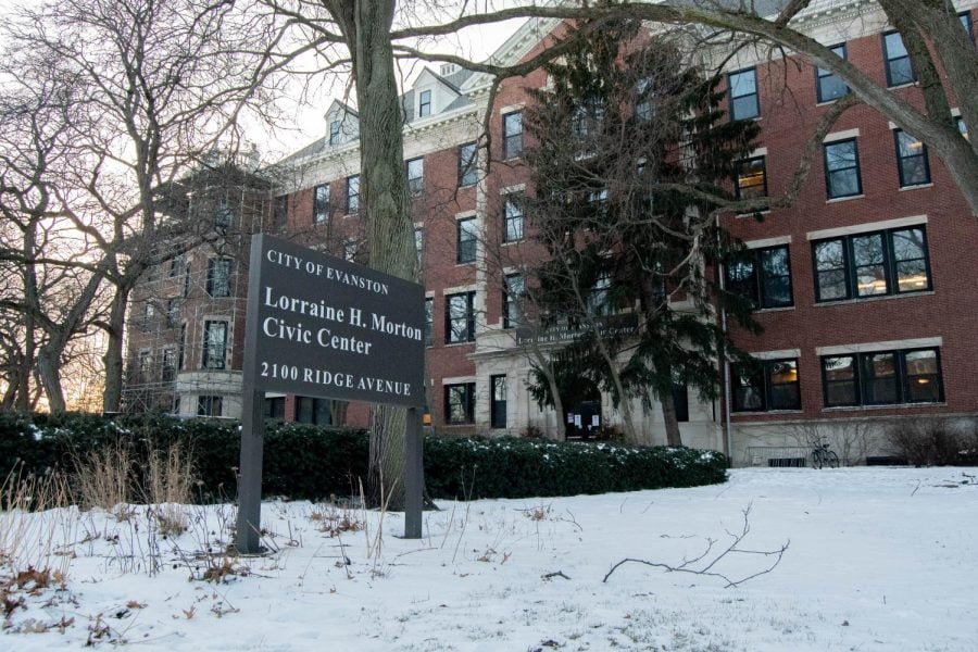The Lorraine H. Morton Civic Center on a snowy day. The walls are a dark red-brown brick and the sign outside is a dark brown. White snow is on the ground and on the trees.