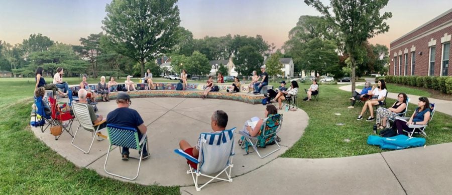 A circle of District 65 parents sit in lawn chairs outdoors.
