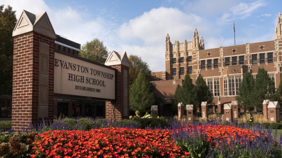 A large brick building with red flowers in front. A large sign reads Evanston Township High School Established 1883.