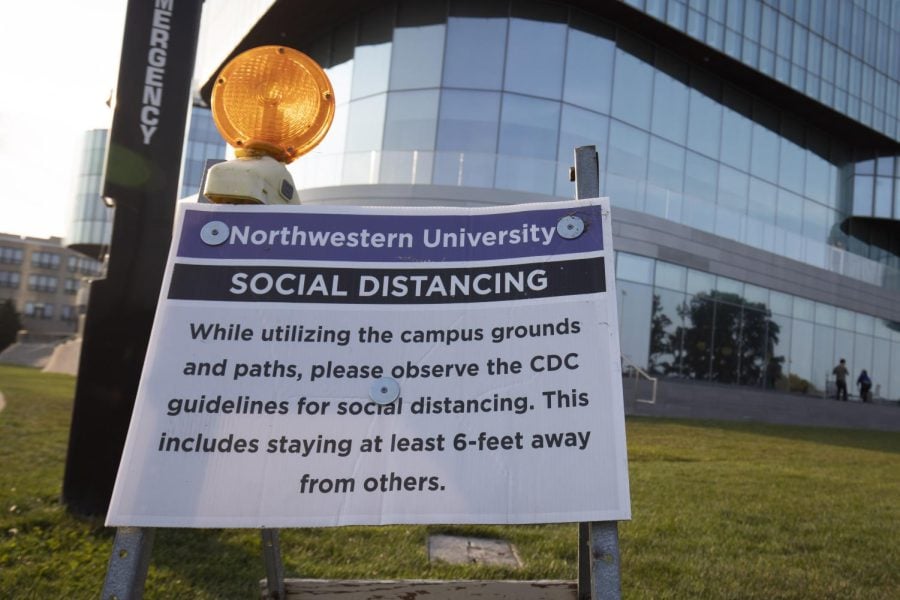 A sign with COVID-19 social distancing protocols in front of a blue building.