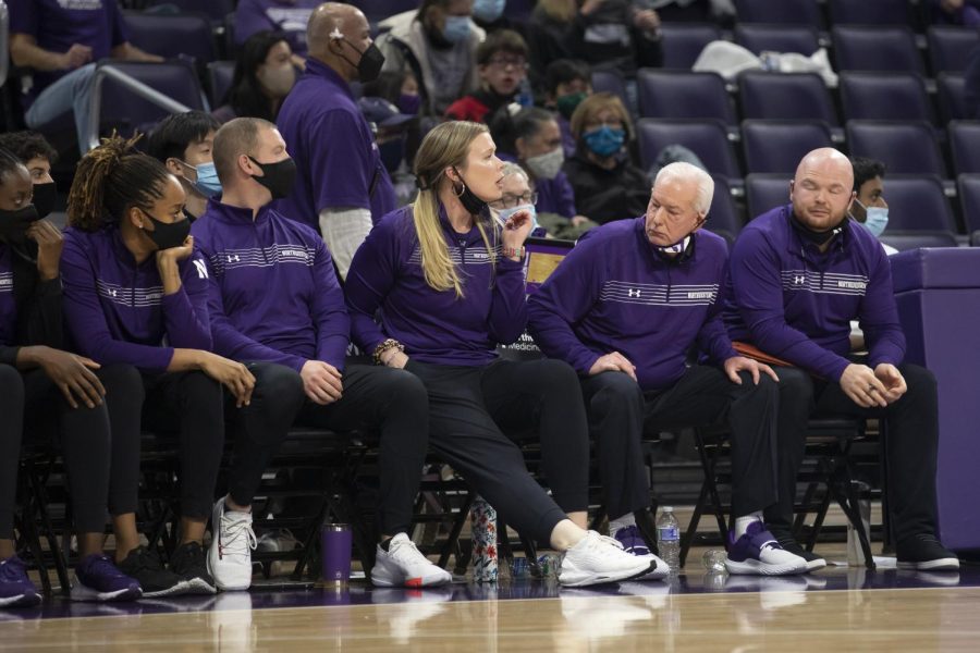 Five Northwestern basketball coaches wearing purple shirts and black pants sit at Welsh-Ryan Arena