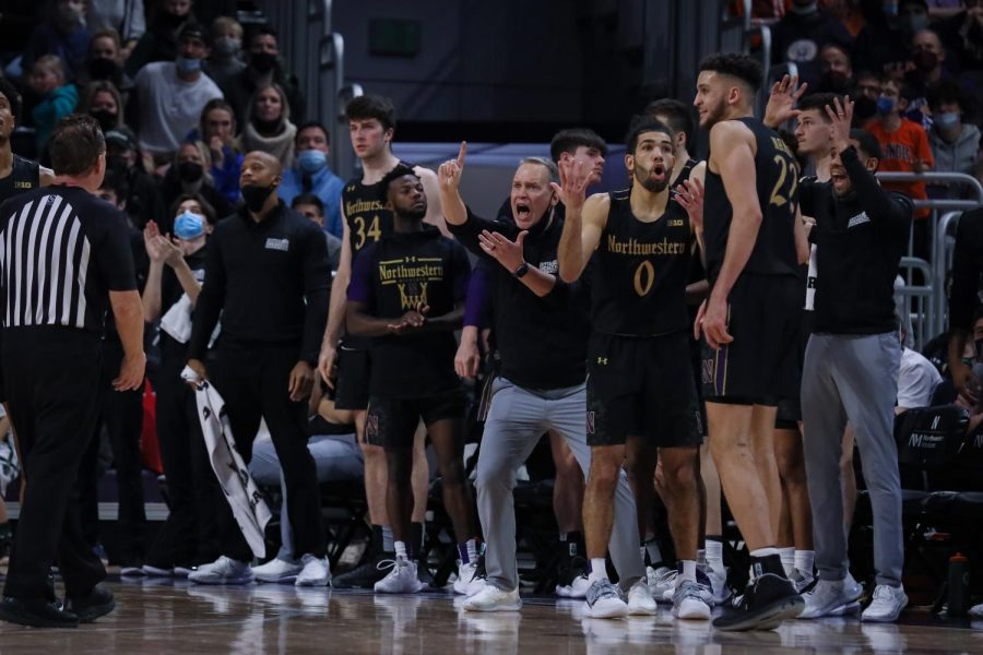 A group of players and coaches on the sidelines of a basketball court yell. 
