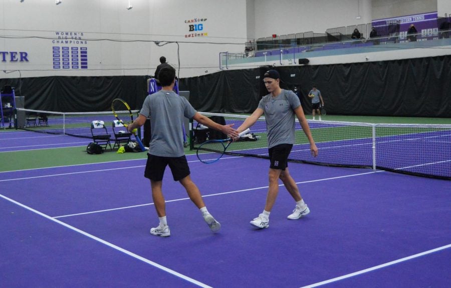 Tennis+players+in+gray+shirt+and+black+shorts+high-five+in+the+middle+of+a+purple+court.