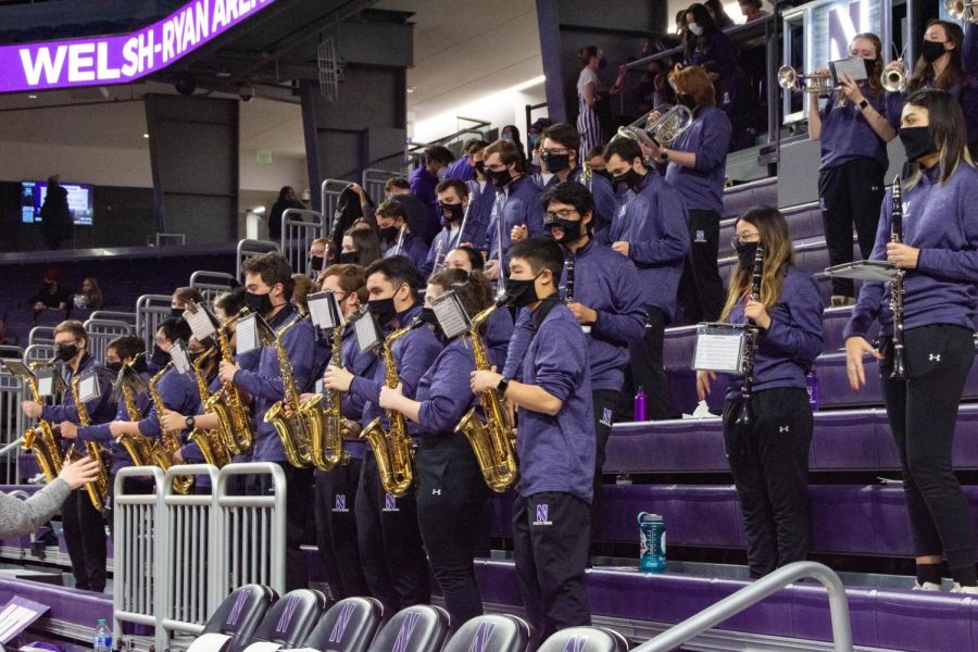 Marching band students in purple shirts play their instruments in the stands.