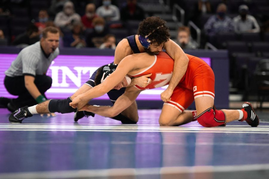 Man in purple singlet wraps his arms around the shoulder of a man in red singlet.