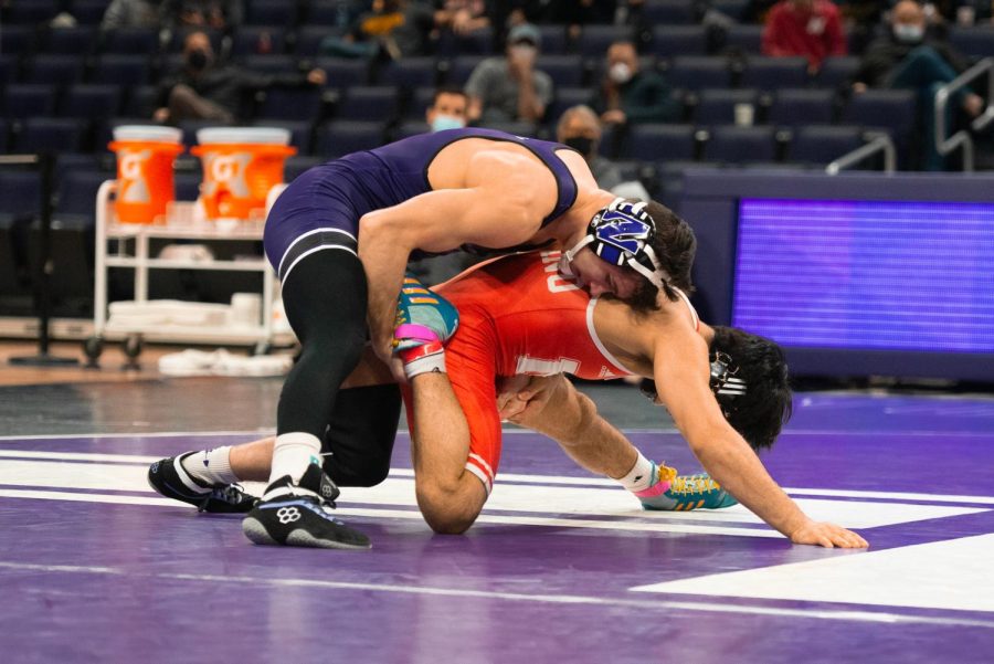 Man in purple singlet wraps his arms around the shoulder of a man in red singlet.
