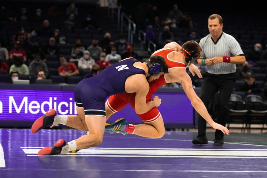 Man in purple singlet wraps his arms around the waist of a man in a red singlet in attempts to complete a takedown.