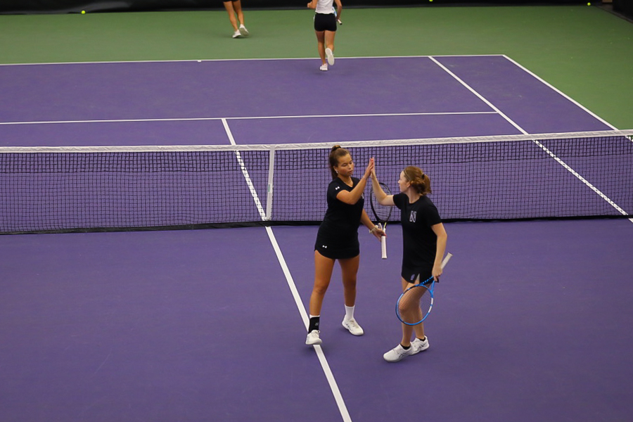 Two+players+in+black+shirts+and+black+shorts+high-five+on+a+purple+court.