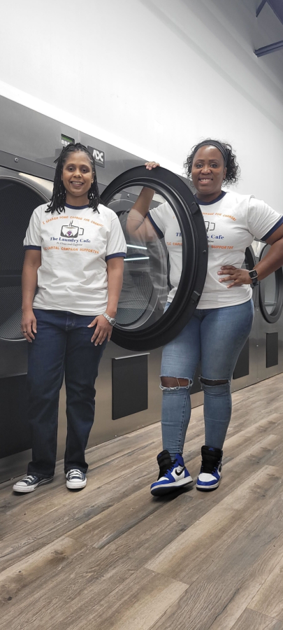 The Laundry Cafe co-creators Jacqui White and Tosha Wilson stand beside a washing machine.