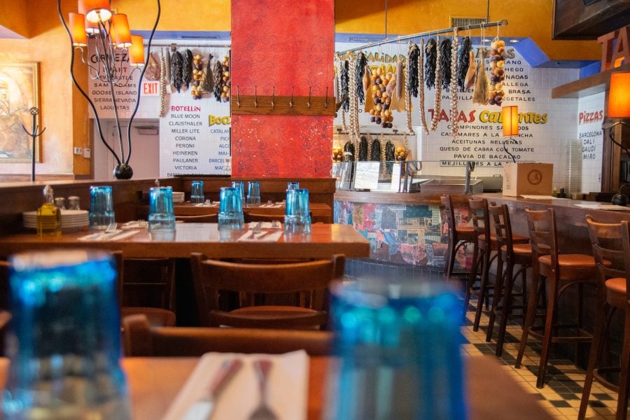 Interior of Tapas Barcelona Restaurant. Blue glasses are placed upside down on tables, and dried spices hang on string from the ceiling. The walls are painted with the restaurants menu.