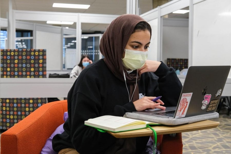 NU student sits at a desk in Main Library looking at a laptop, with a notebook open on the desk.