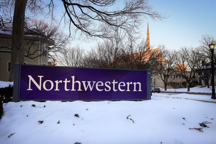 A Northwestern sign rests surrounded by snow with university buildings in the background.