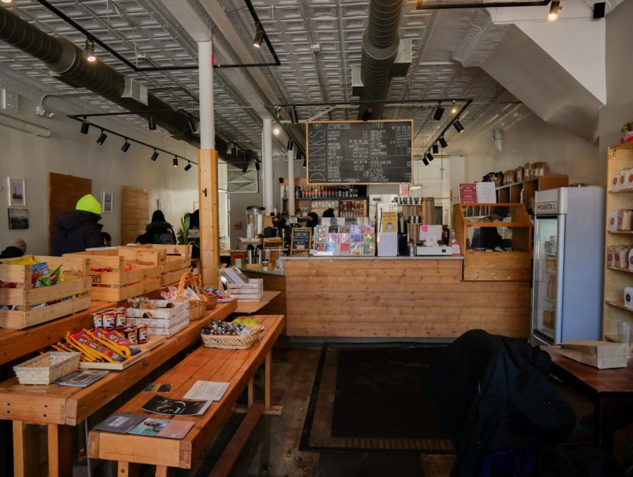 The front entry of the coffee shop. There is a wooden ordering counter and a hanging menu sign. On the left is a wooden table with snacks for sale.