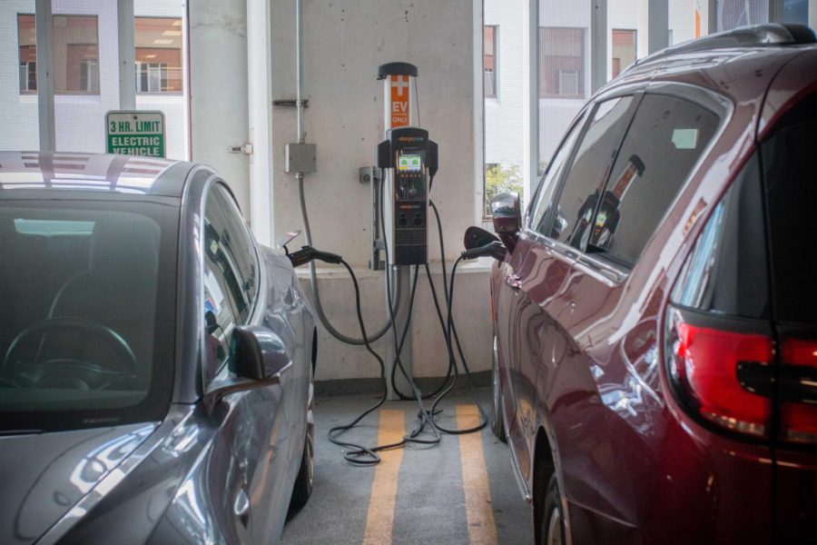 A red and a gray car are hooked up to an electric vehicle charging station inside a parking garage.