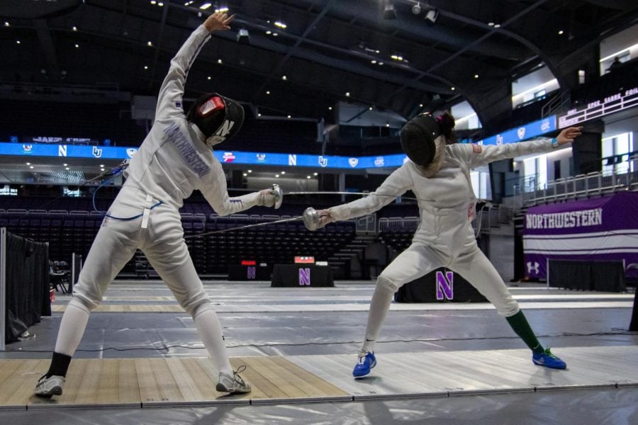 The fencer on the left extends their arm over their head while pointing their fencing weapon towards their opponent.