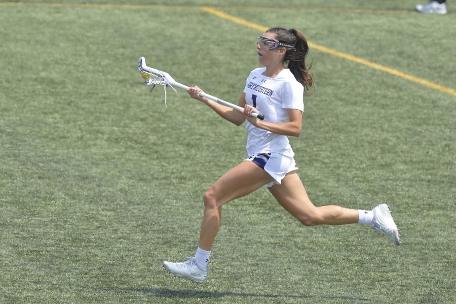 A lacrosse player wearing white holds her stick and runs