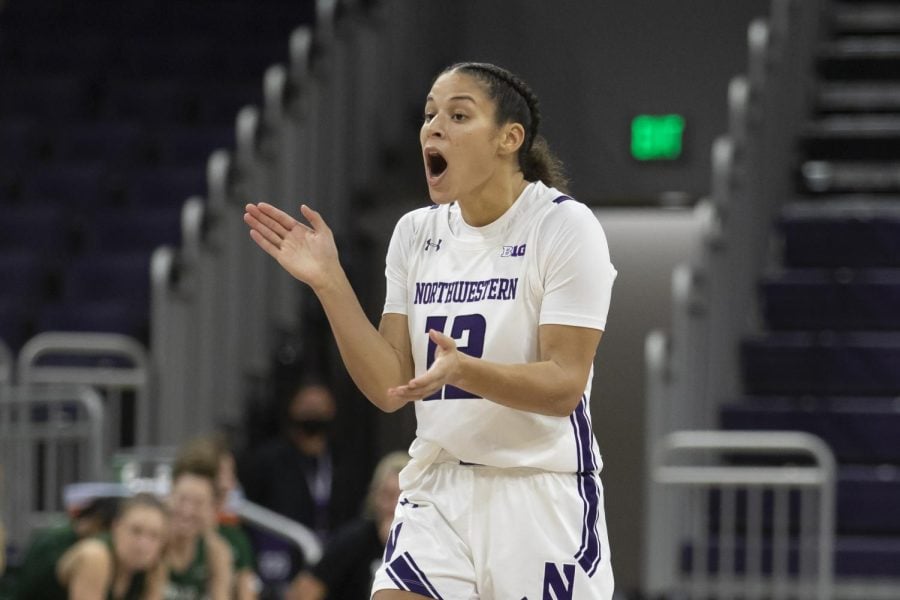 A woman basketball player in a white and purple jersey claps