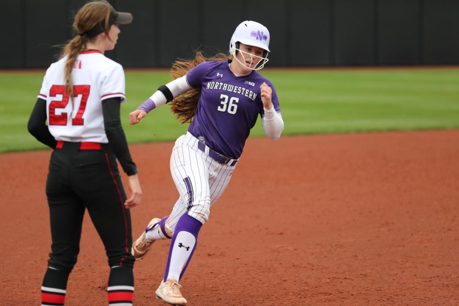 Softball player in purple and white uniform runs around the bases on a field.