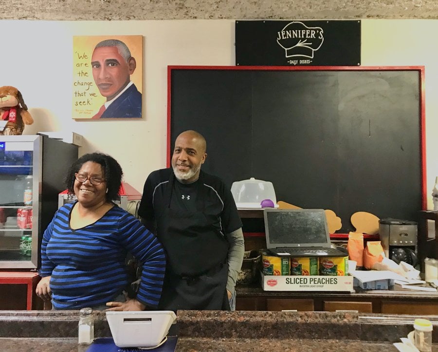 Jennifer’s Edibles owner Jennifer Eason (left) and her brother and former managing partner William Eason (right) stand behind the counter at the restaurant. A painting of former President Barack Obama with the quote “we are the change we seek” hangs behind them on the wall. A blank chalkboard also lines the wall behind them.