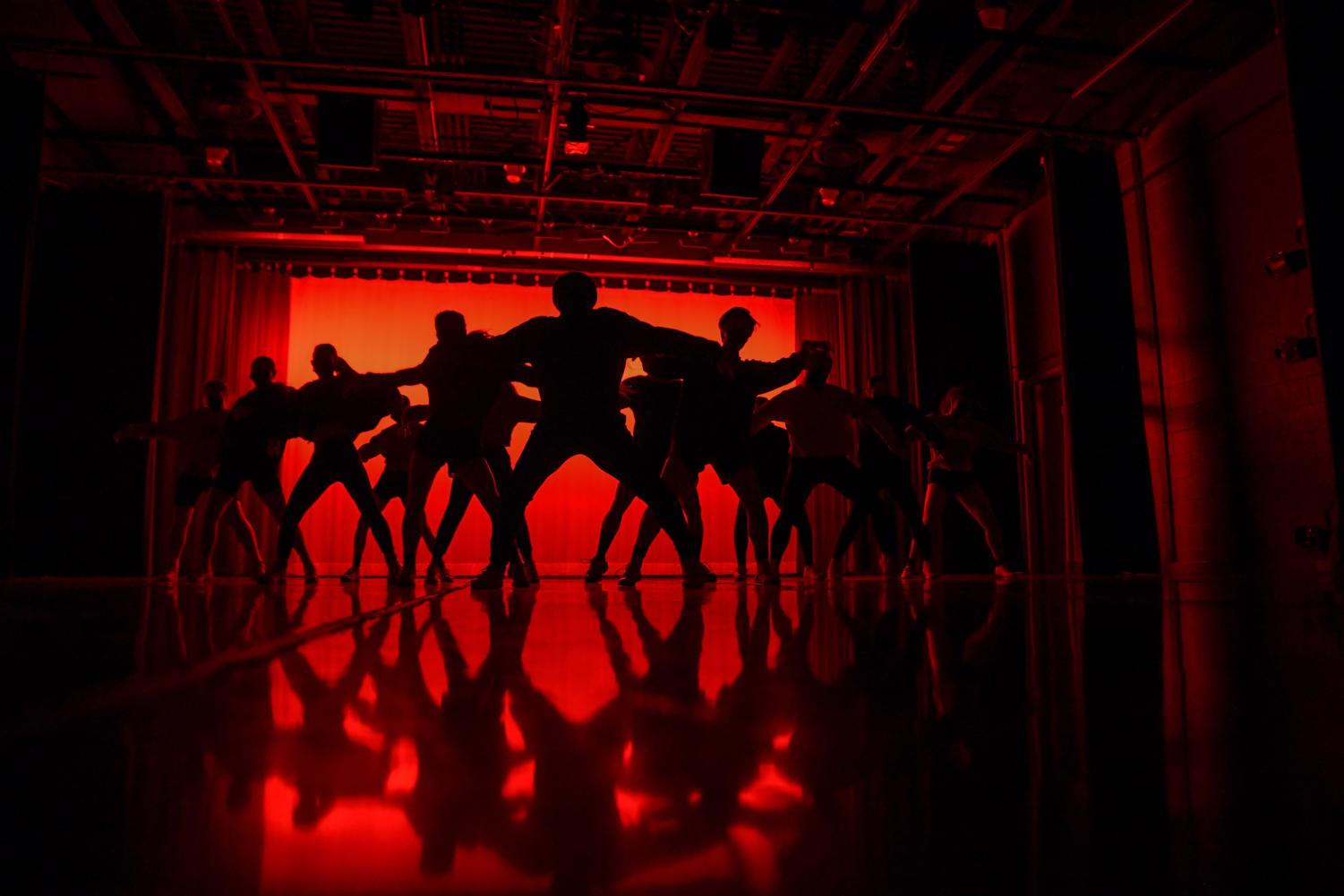 Silhouetted+dancers+in+front+of+a+red+backdrop+squat+at+the+beginning+of+their+dance.