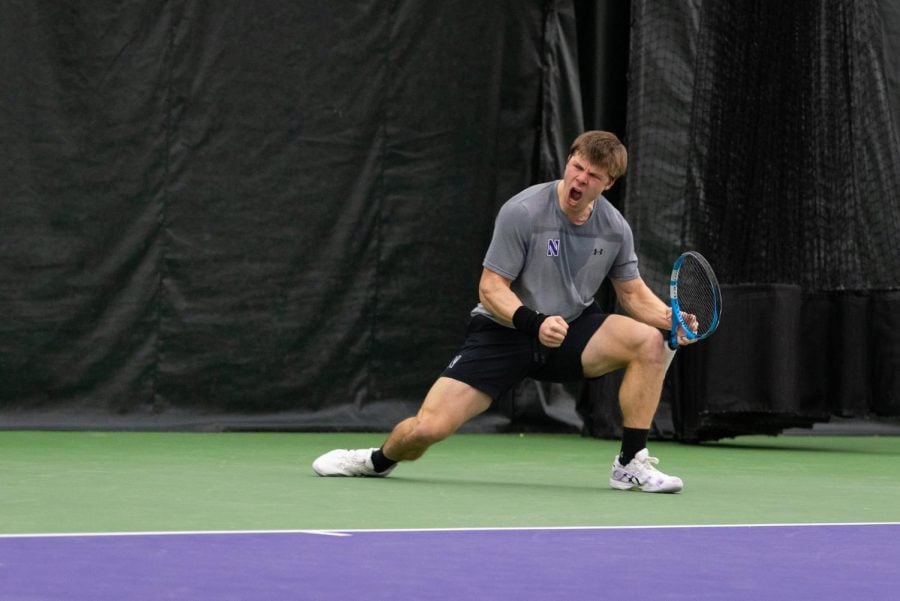 Open-mouthed tennis player in gray shirt, white shoes and black shorts pumps fist.