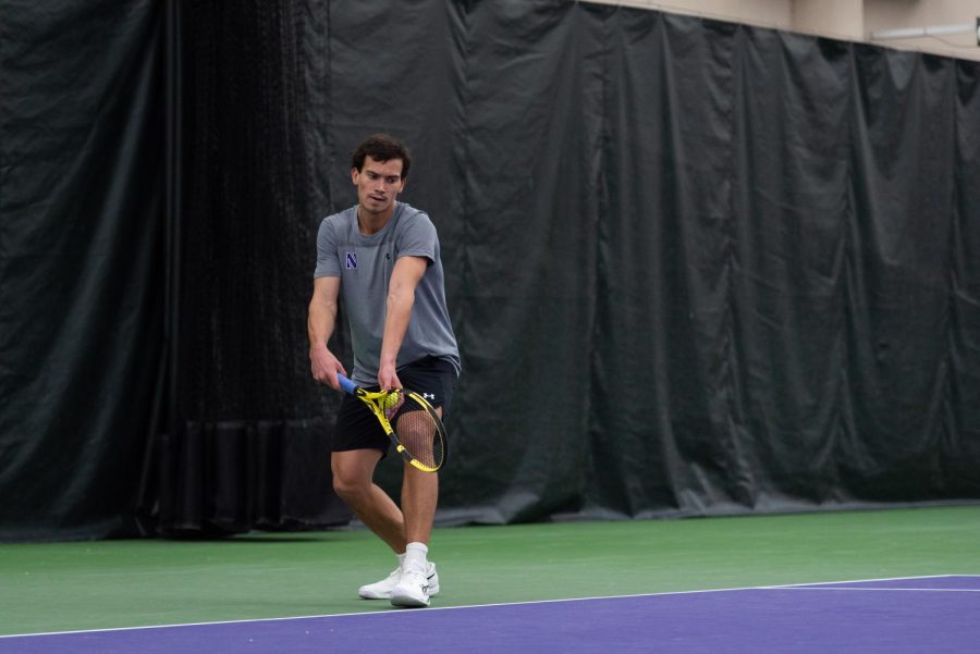 Male+tennis+player+in+gray+shirt+and+black+shorts+holds+tennis+ball+and+racquet+to+serve
