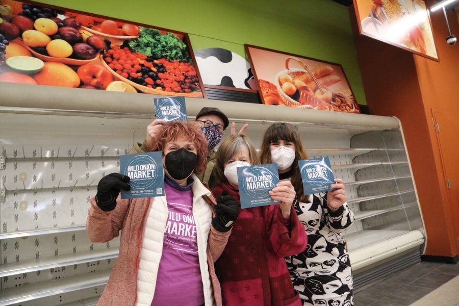 Michelle Parker-Katz, Ricky Burton-Romero, Mary Meyer, and Brooke Langton pose in face masks with branded “We’re an owner!” Wild Onion Market fliers in the co-op’s new location.