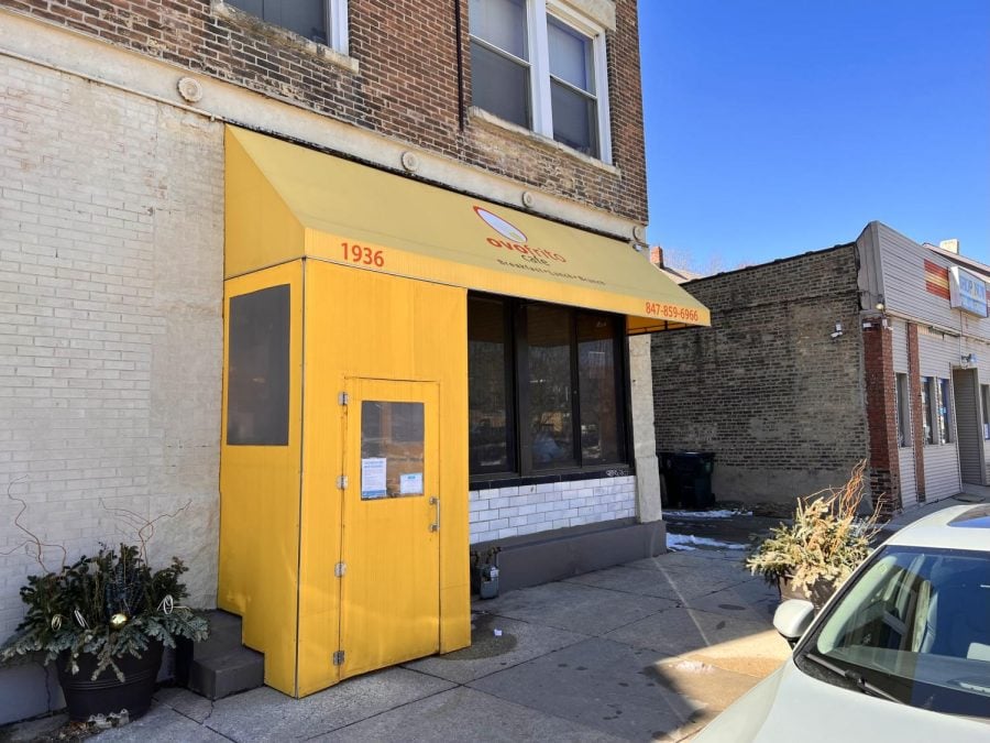 Photo of Ovo Frito Cafés exterior. A bright yellow awning and doorway take center frame.
