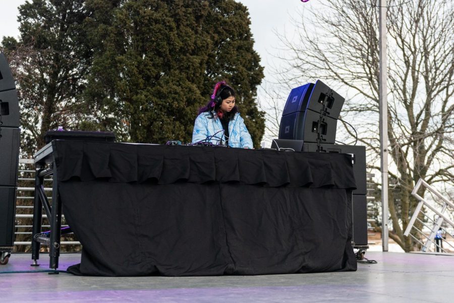 A woman with black and pink hair and blue jacket DJs on stage.