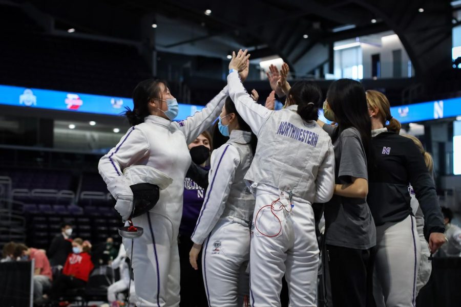 Several fencing team members gather together and high-five.
