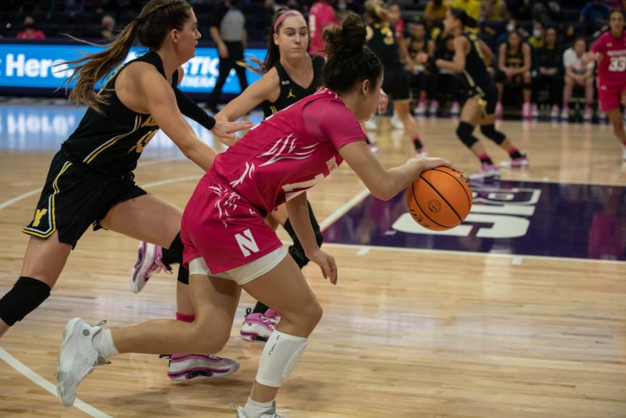 Girl in pink uniform with hair in a bun dribbles ball.