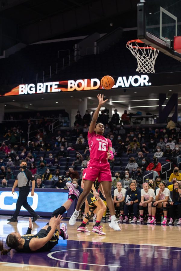 Woman basketball player wearing a pink uniform goes up for a right-handed shot in the air