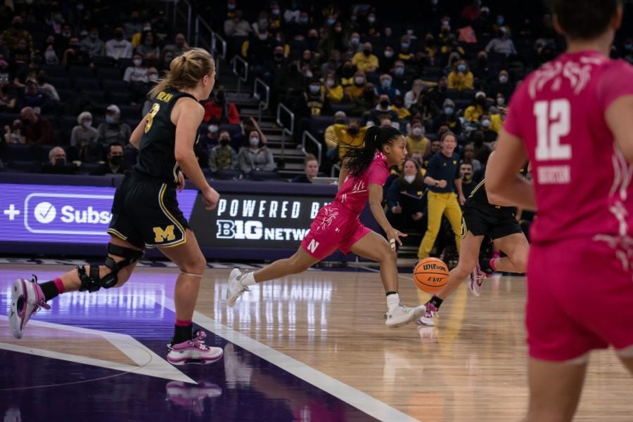 A person in a pink jersey runs and dribbles a basketball alongside two people in black jerseys.