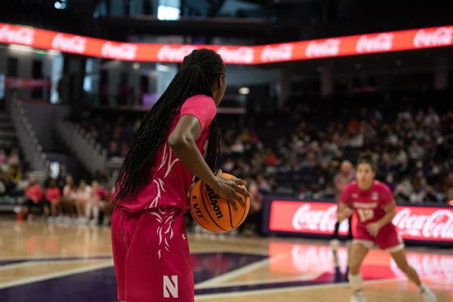 A person in a pink jersey holds a basketball and looks at another person in a pink jersey. 