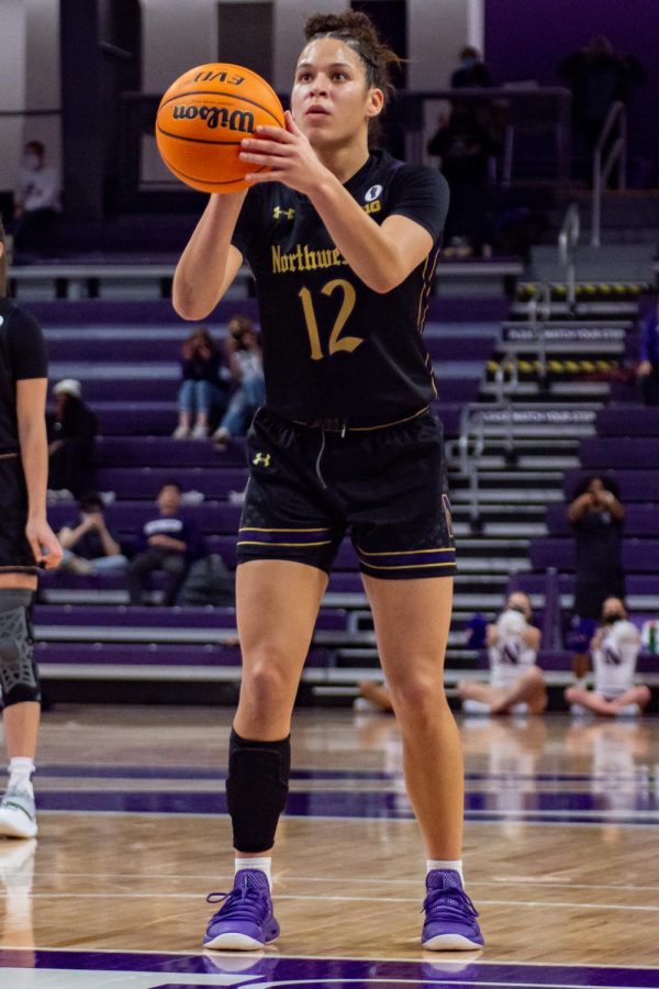 A woman basketball player in a black uniform and purple shoes shoots a free throw