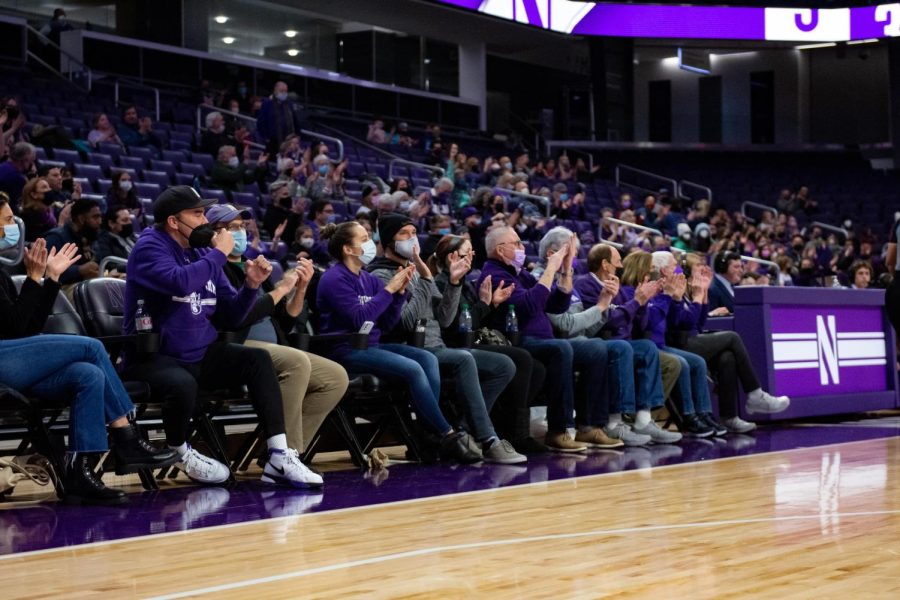 Individuals in purple attire cheer on the side of the basketball court.