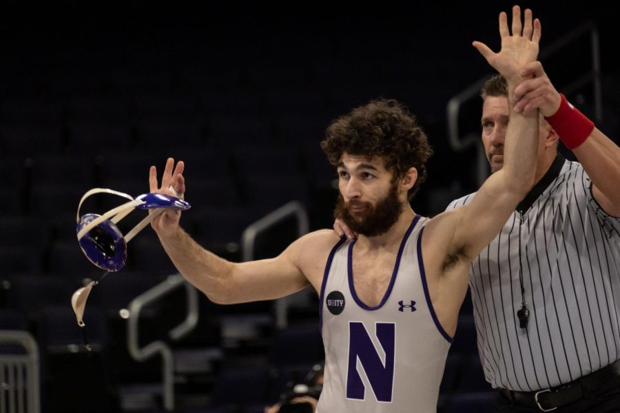 A wrestler raises both arms. A referee is behind the wrestler and holds their left hand up.