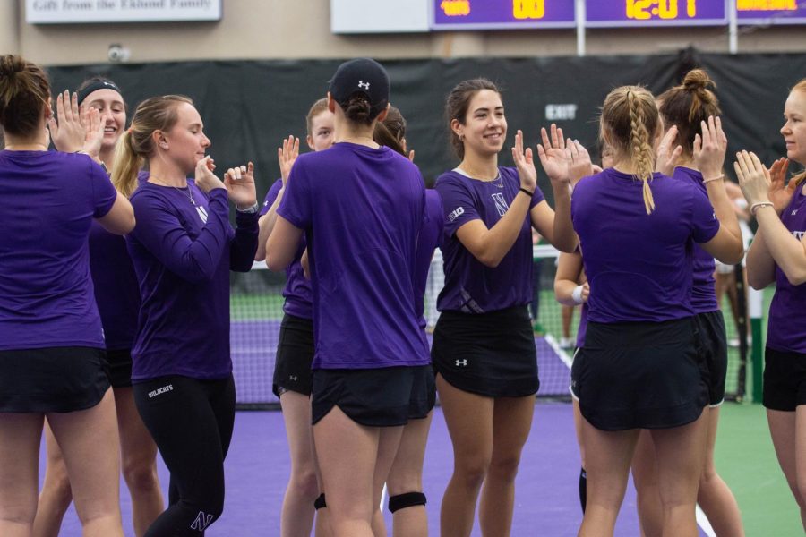Several tennis players in purple shirts high five each other, smiling.