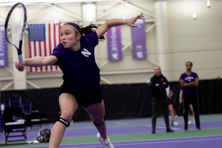 A tennis player in a purple shirt dives forward to hit a ball with her tennis racket.