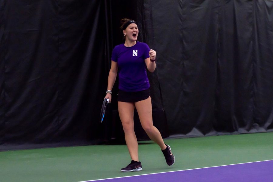 A tennis player in a purple shirt and black shorts fist pumps.