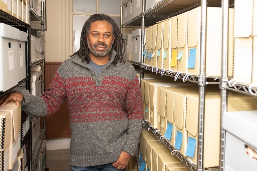 Dino Robinson Jr. stands between two shelves of archival documents.