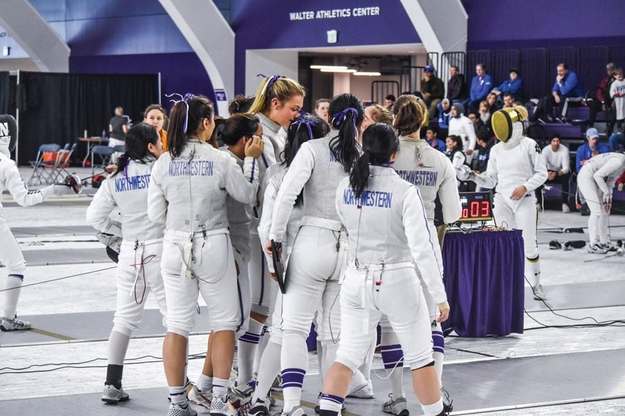 The fencing team, wearing white suits, huddle together.