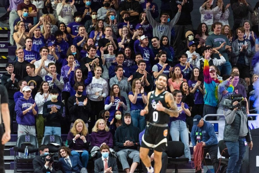 Many people cheer for a basketball game. A player in a black jersey is out of focus in the foreground. 