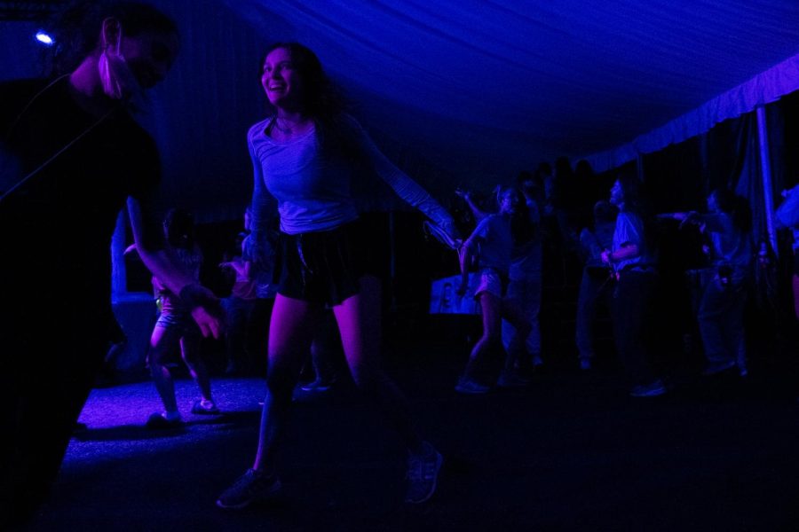 Students dance in a tent with blue lights shining.