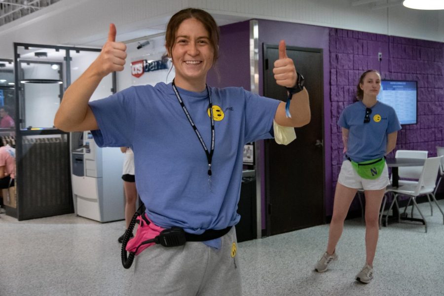 A student in a blue shirt poses for a picture with their thumbs up.