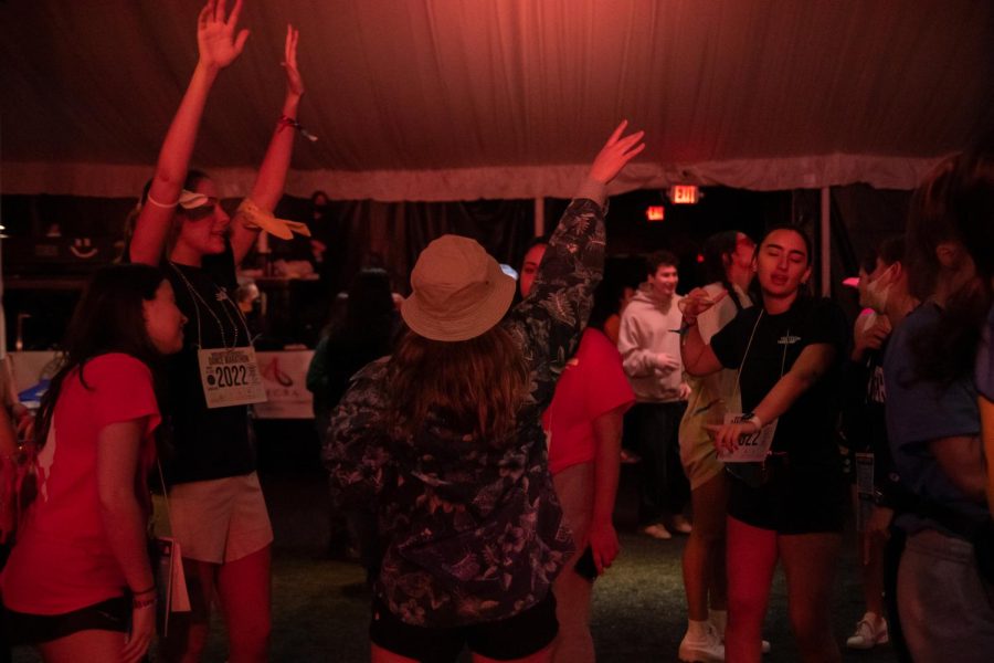 Several students dance with their arms up in the tent.