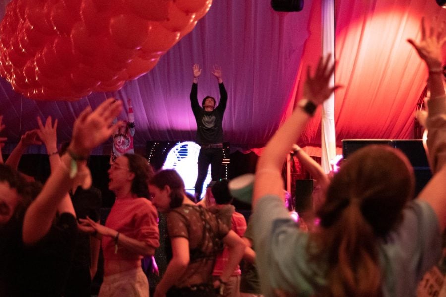 Students hold their arms up with the music in a tent. Someone on stage does the same.